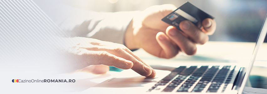 Persoană utilizând un card bancar pentru efectuarea unei plăți pe un laptop și logo-ul CazinoOnlineRomânia.ro